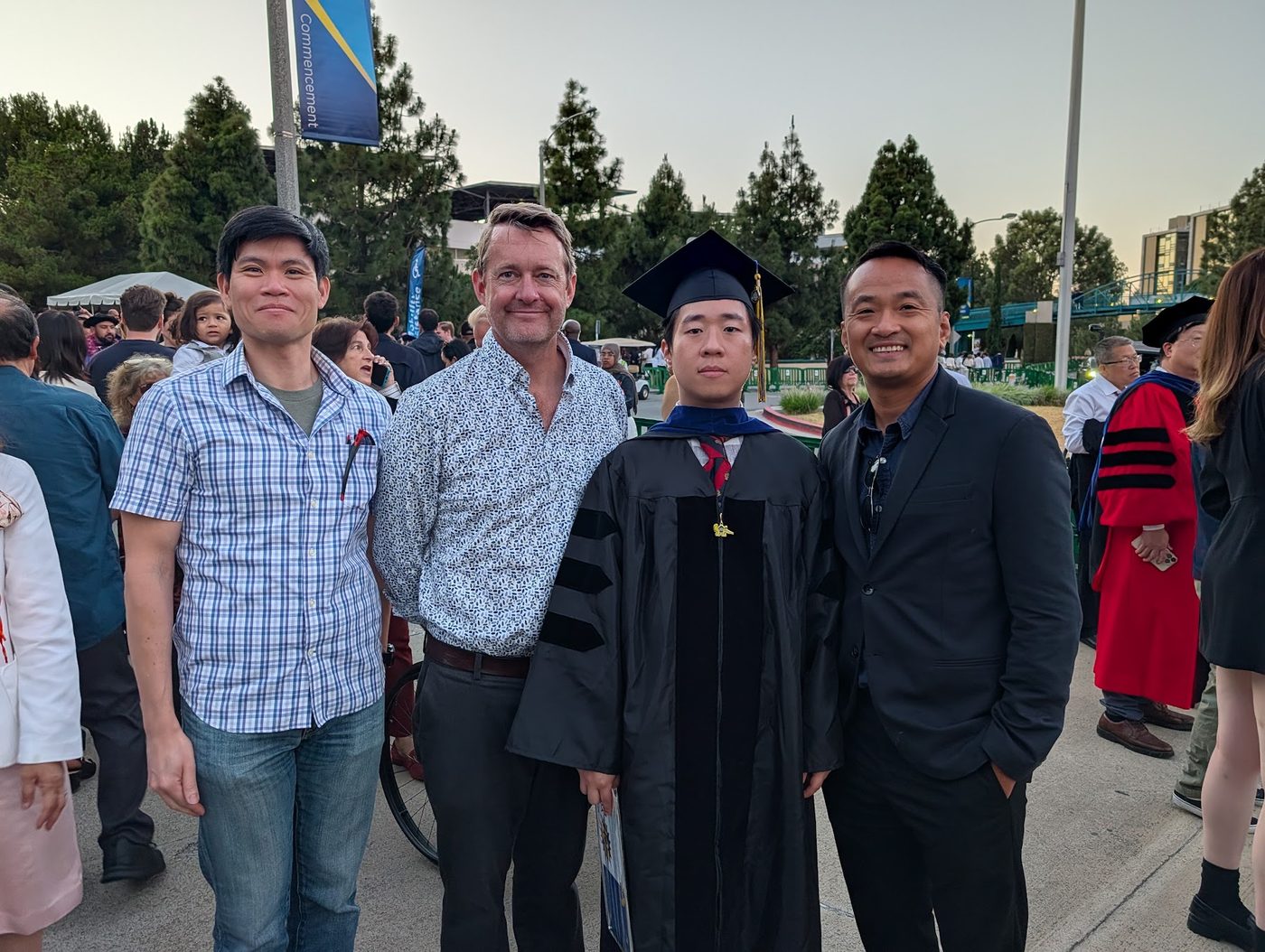 Daeyun Shin in doctoral cap and gown at UC Irvine commencement, standing with three colleagues on either side of him.